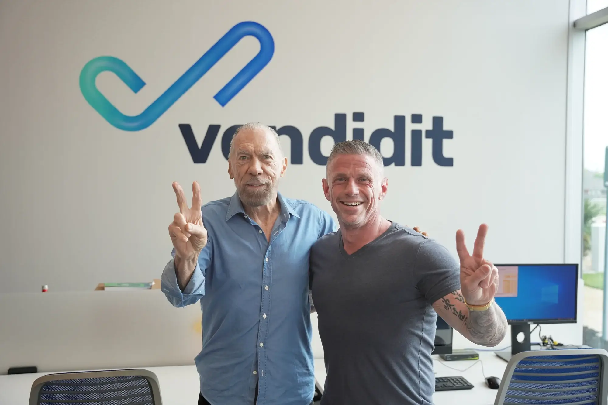 Two men posing with peace signs in front of the Vendidit logo.