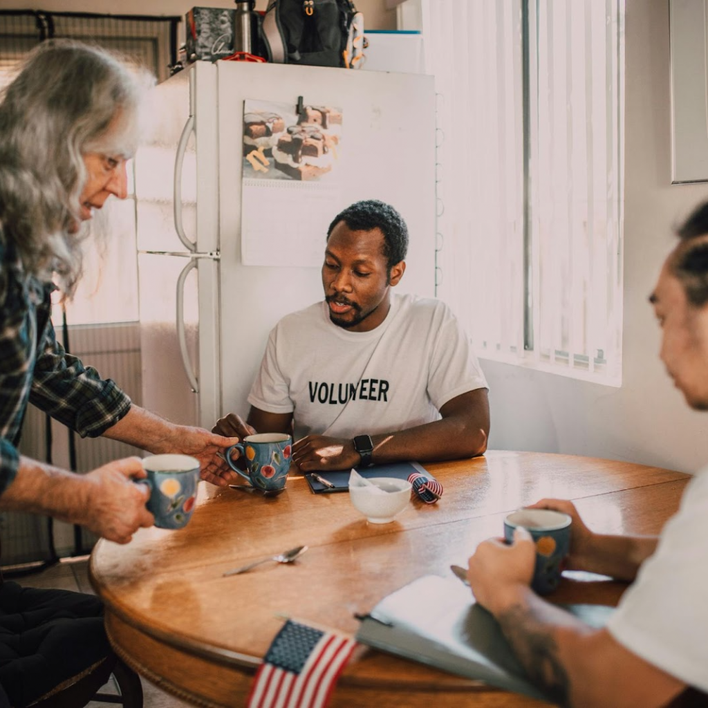 Volunteer sharing coffee and conversation with veterans at a kitchen table, showing support and connection.